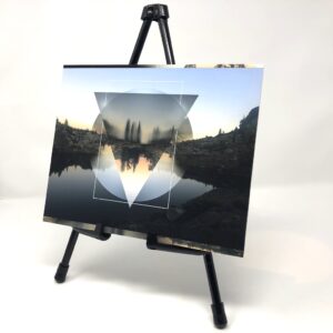 Fine art print displayed on a black easel featuring a sunset photograph of Downey Lake near Lake Tahoe, California, with layered geometric shapes over the landscape reflection.
